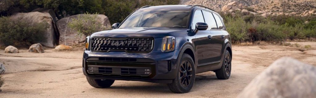 Dark blue SUV parked on a dusty, rocky terrain with large boulders and sparse greenery, shown from a front three-quarter angle.
