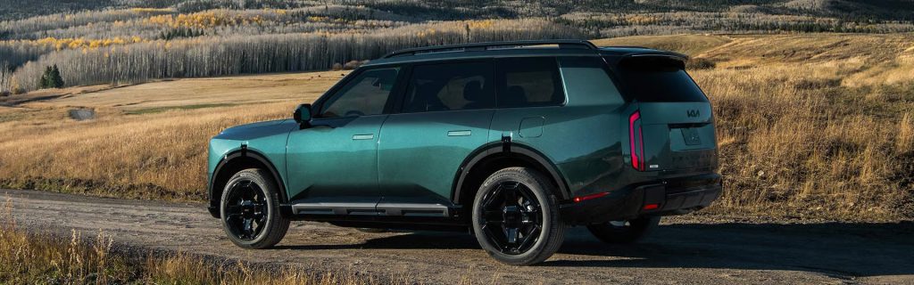Green Kia Telluride SUV parked on a scenic countryside road, showcasing its bold design against a picturesque mountain landscape.